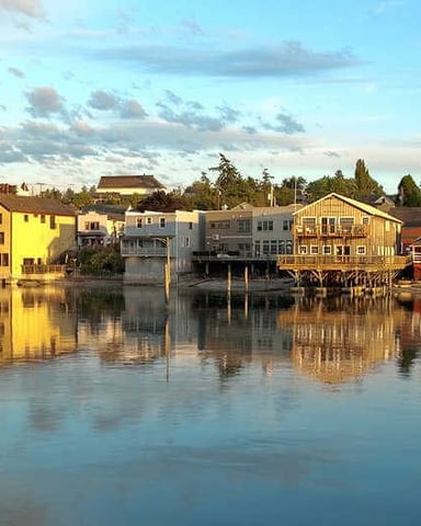 Waterfront buildings and docks reflected in calm water under partly cloudy sky