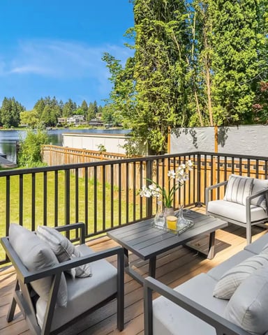Waterfront deck with lounge seating, black railing, and view of lake surrounded by evergreen trees