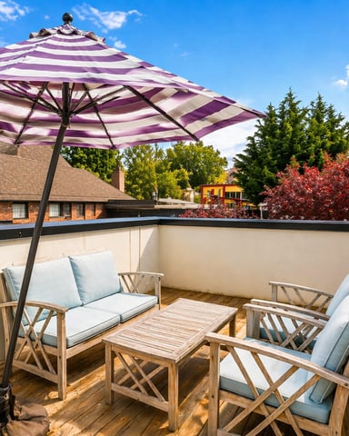 Rooftop deck with purple striped umbrella, wooden furniture with blue cushions, and views of neighboring brick homes and trees
