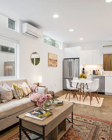 Open-plan living room and kitchen with beige sofa, wooden coffee table, white cabinetry, stainless steel appliances, and dining area.