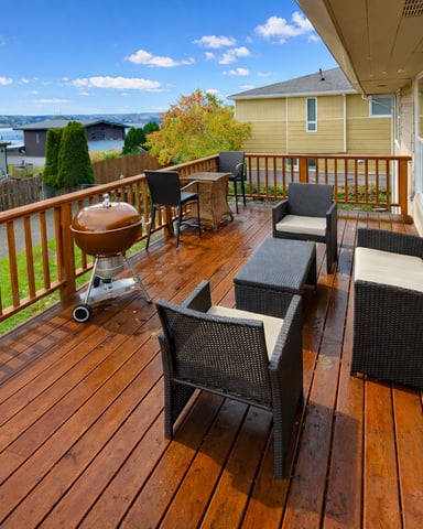Wooden deck with wicker seating, grill, and water view overlooking residential neighborhood