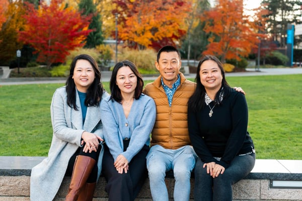 Four people sitting on a concrete bench in a park with autumn foliage in the background