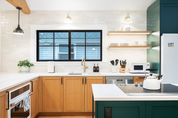 Modern kitchen with wood cabinets, white countertops, black-framed window overlooking water, open shelving, and green island