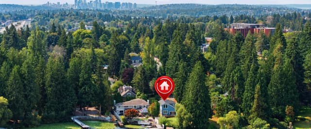 Waterfront home with red location pin marker, surrounded by evergreen forest with city skyline in distance